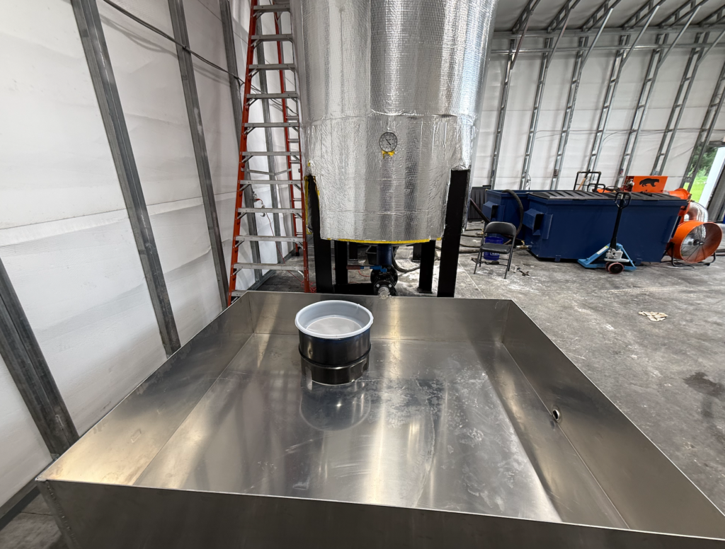 Stainless steel used cooking oil processing tank with industrial ventilation equipment inside a recycling facility.