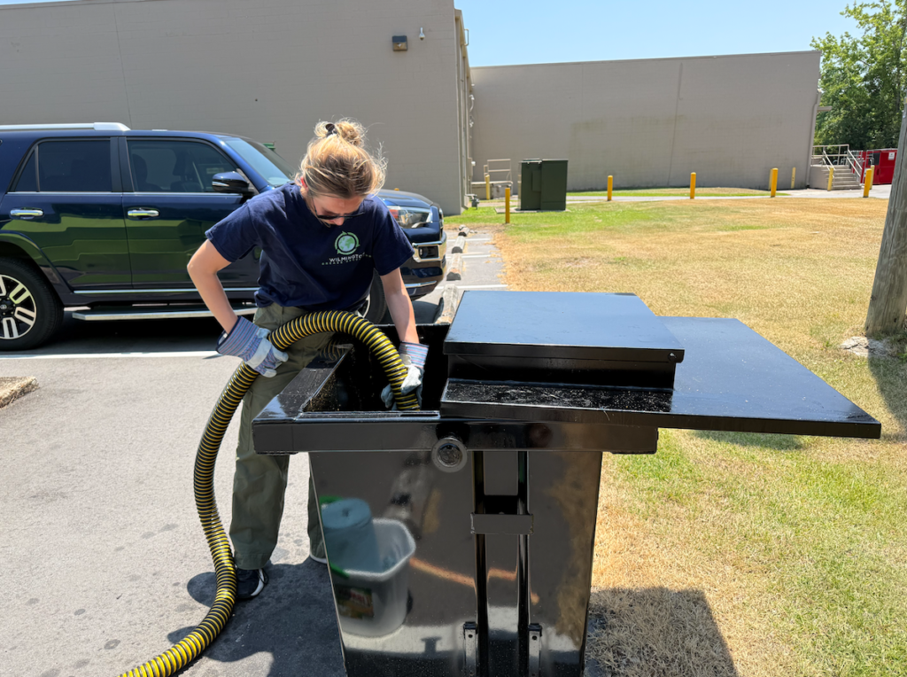 Worker using a hose to collect used cooking oil from a commercial grease recycling container outdoors.